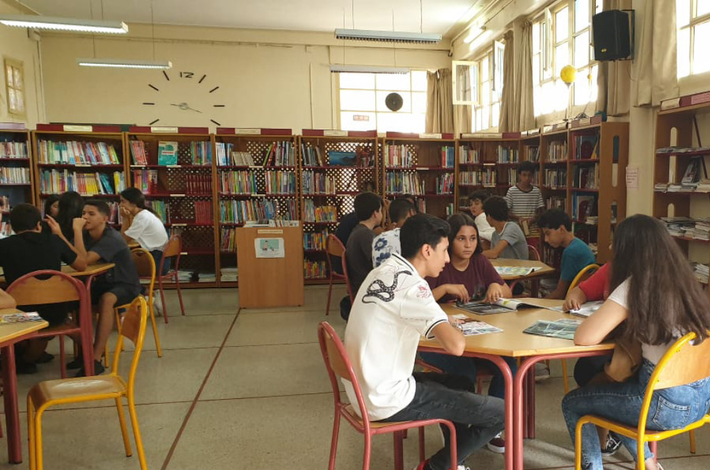 High school students sitting around tables, in the school library